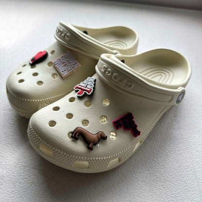 A pair of beige Crocs shoes with various charms attached to them, including a Muay Thai inspired design.